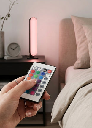Barra LED RGB na mesa, a emitir luz rosa, com comando à distância na mão.