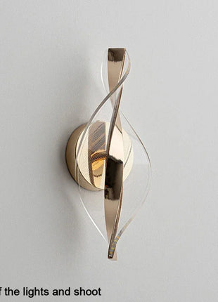 Aplique de parede LED dourado com estrutura metálica em espiral e luz acesa.