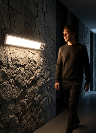 Barra LED com sensor PIR, acesa numa parede de pedra, feixe branco.